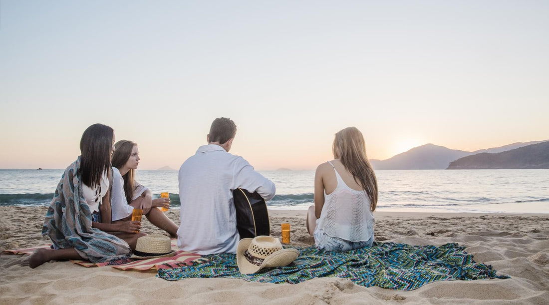 Group of friends, one male and three females enjoying a relaxing evening at the beach, they are comfortably settled on sand-free beach towels