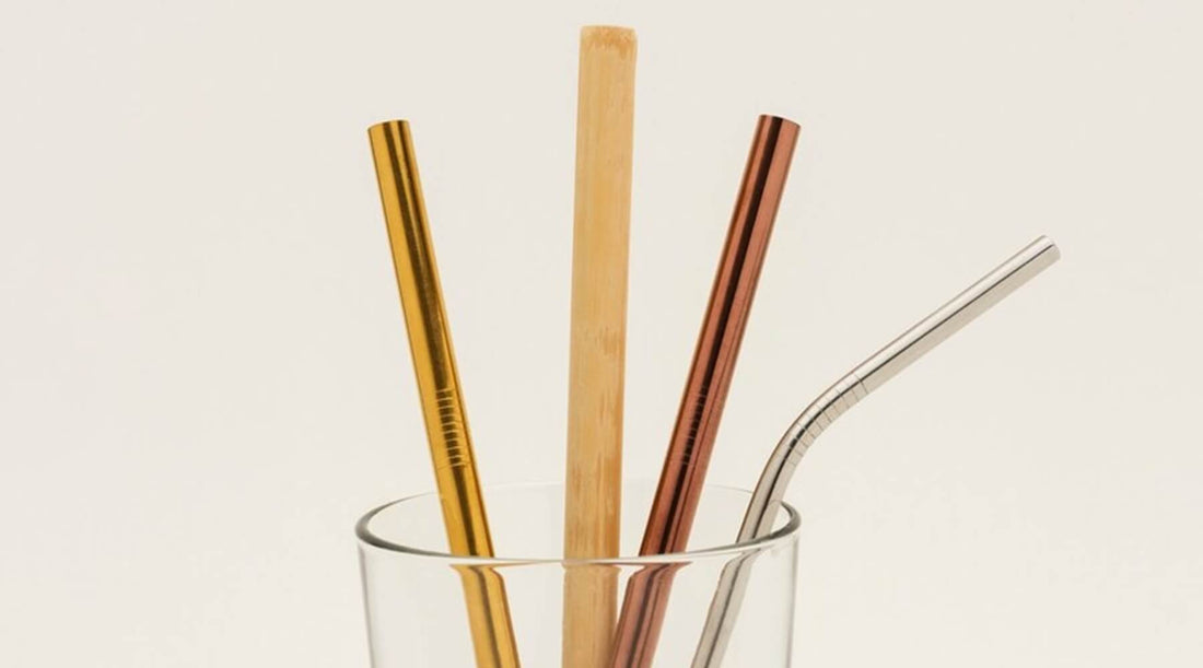 Four reusable straws in a glass on a white background. The straws appear to be eco-friendly straws made from different materials, including metal, bamboo, and glass