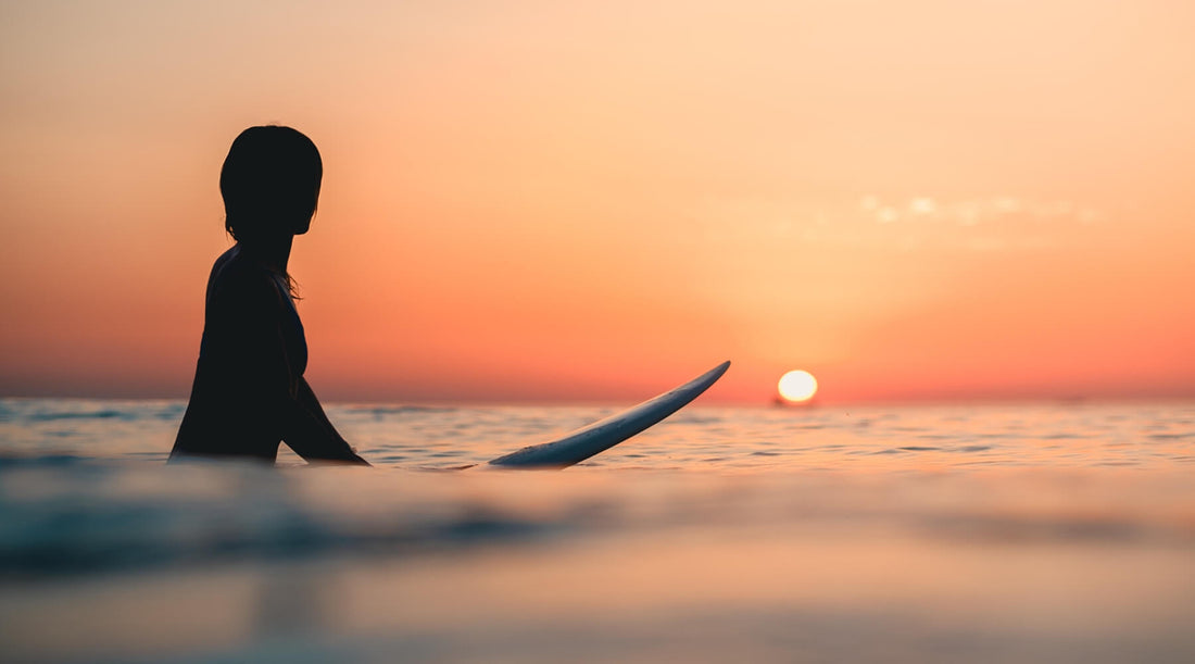 A lone surfer paddles on their board across the ocean, bathed in the vibrant colors of a stunning sunset